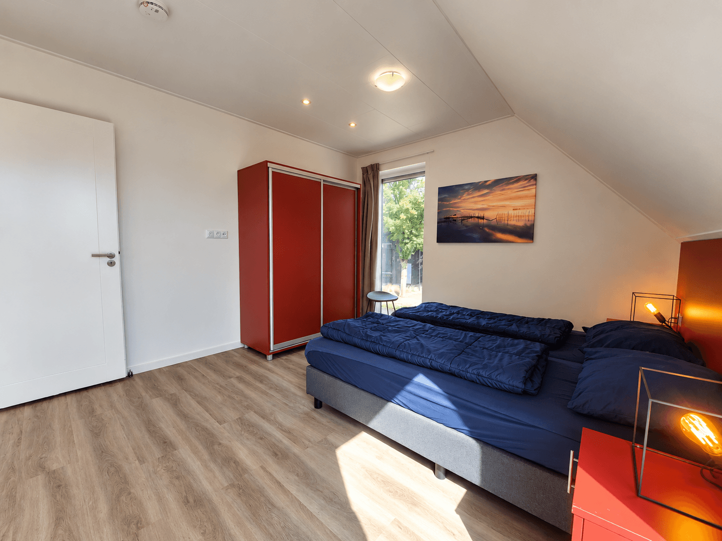 Slaapkamer met een tweepersoonsbed, kast in rode kleur en een venster met uitzicht op de tuin.