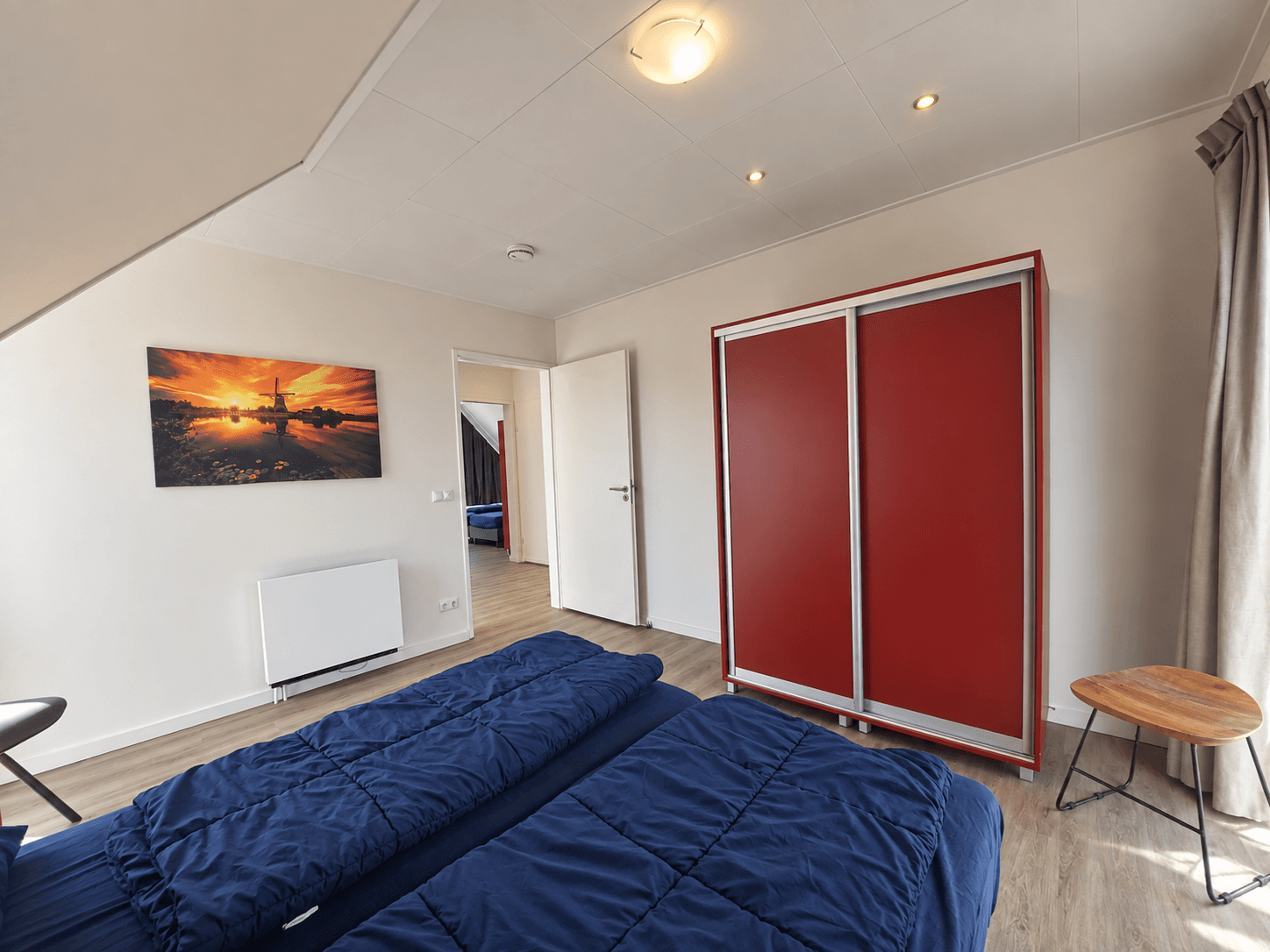 Slaapkamer met twee aparte bedden, een rode kast, een schilderij en een raam met zicht op de buitenruimte.