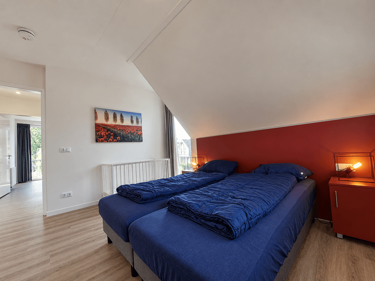 Slaapkamer met twee eenpersoonsbedden, een rode wand en een schilderij met landschap aan de muur.