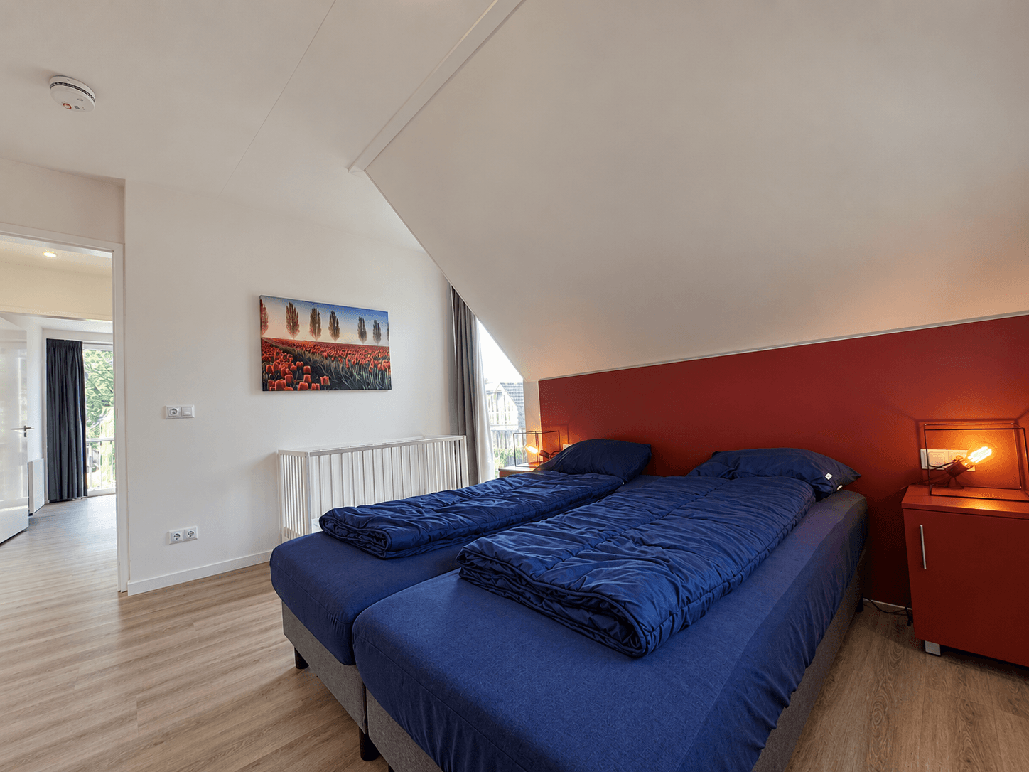 Slaapkamer met twee eenpersoonsbedden, een rode wand en een schilderij met landschap aan de muur.