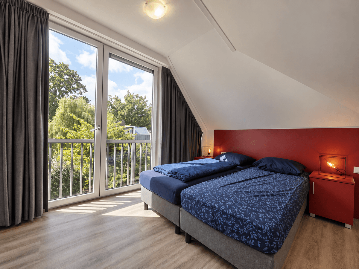 Slaapkamer met twee eenpersoonsbedden en een balkon met uitzicht op groene bomen