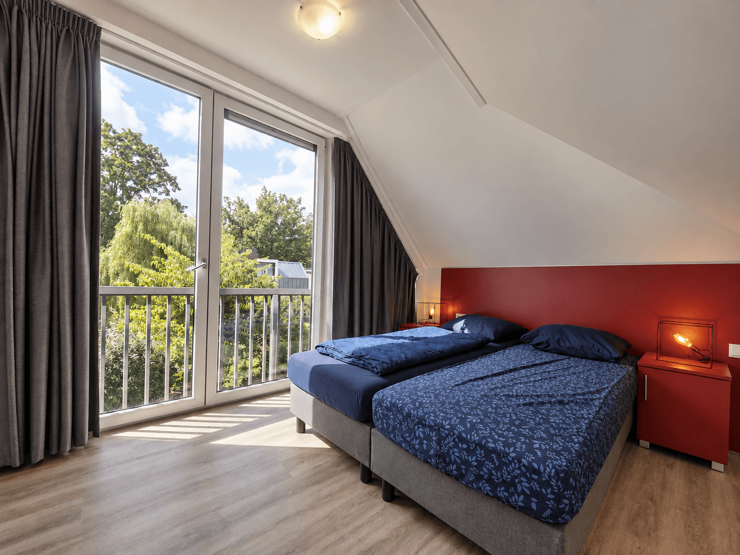 Slaapkamer met twee eenpersoonsbedden en een balkon met uitzicht op groene bomen
