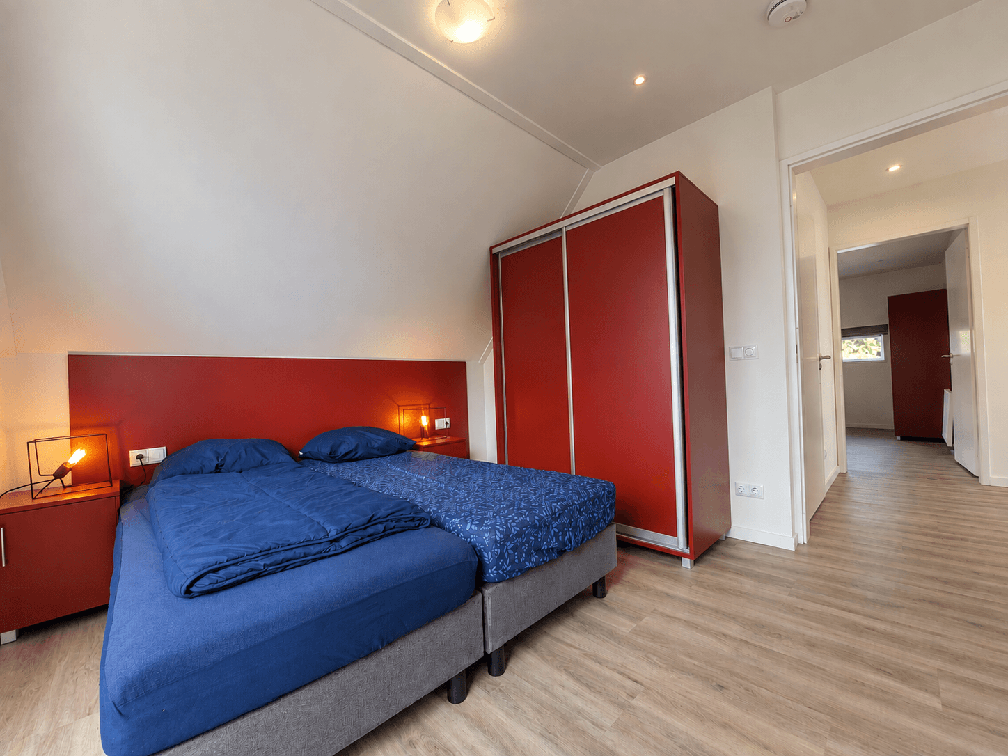 Slaapkamer met twee eenpersoonsbedden en een kast, muren en meubels in neutrale en rode tinten