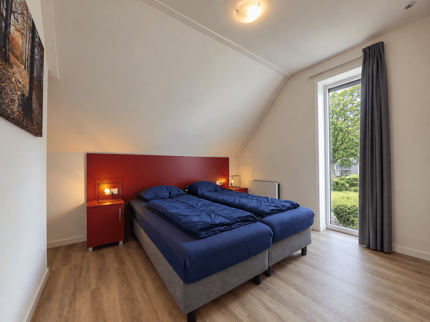 Slaapkamer met twee eenpersoonsbedden, nachtkastjes met lampen en een raam met uitzicht op de groene omgeving.