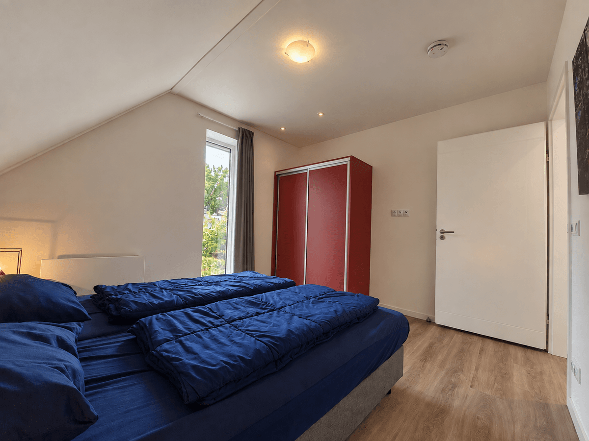 Slaapkamer met twee eenpersoonsbedden, een rode kast en een raam met zicht op buiten.