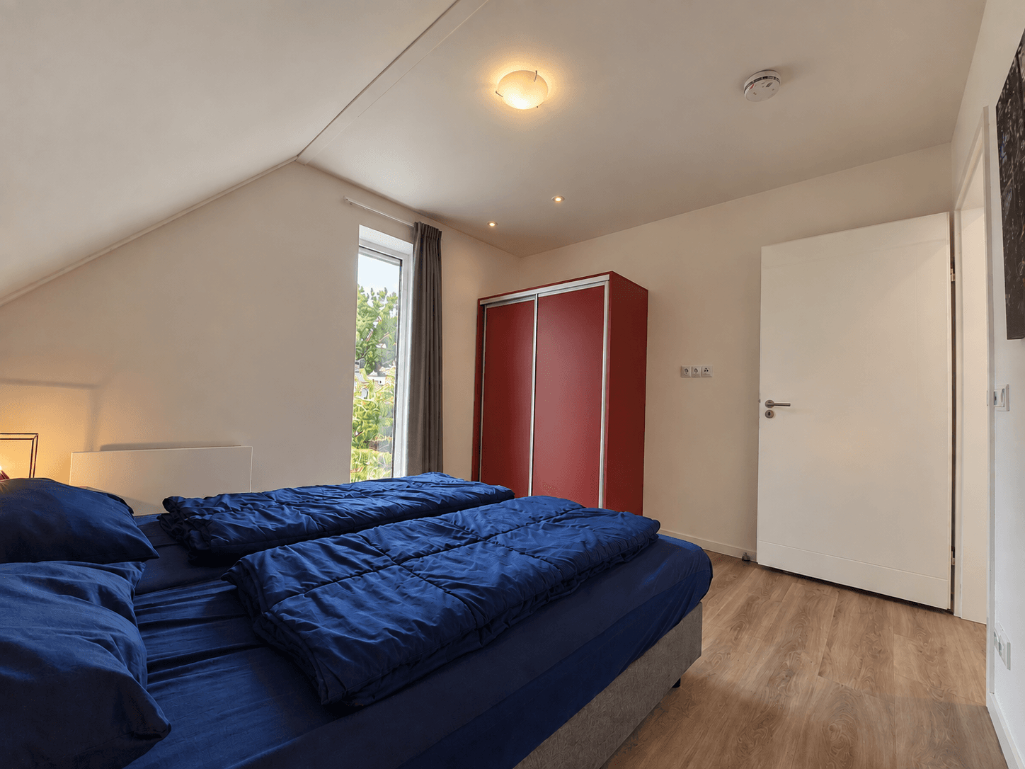 Slaapkamer met twee eenpersoonsbedden, een rode kast en een raam met zicht op buiten.
