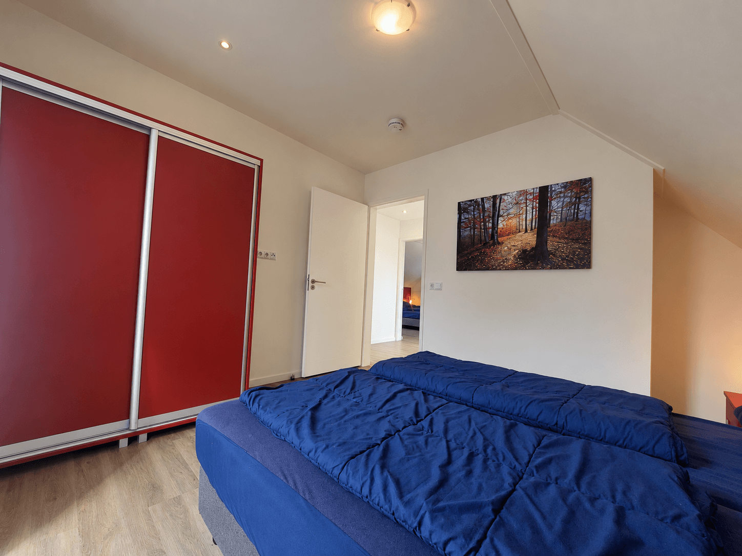 Slaapkamer met een tweepersoonsbed, kast met rode schuifdeuren en een schilderij aan de muur
