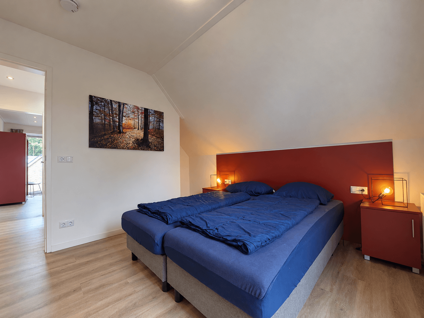 Tweepersoonsbed met blauwe dekbedden en nachtkastjes in een lichte slaapkamer met moderne inrichting.