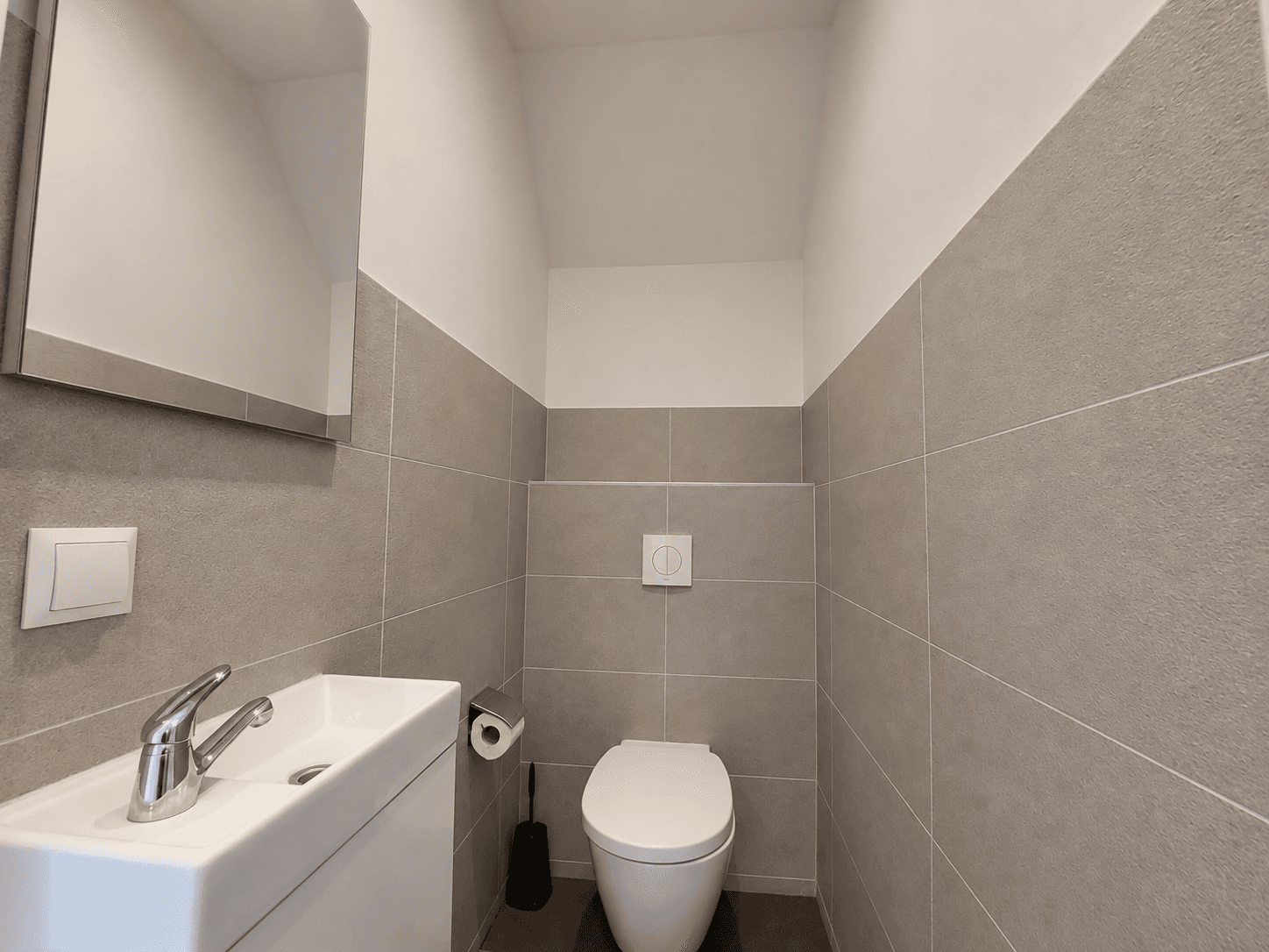 Wc met modern sanitair, wastafel en grote spiegel, betegelde wanden in neutrale kleuren