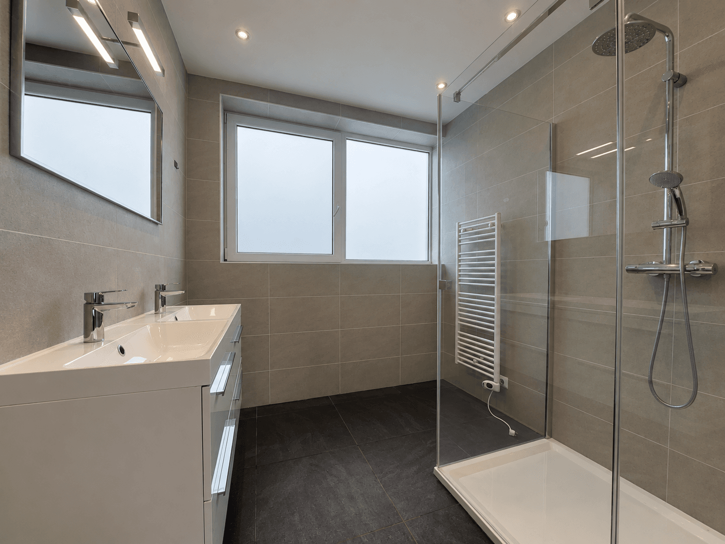 Moderne badkamer met dubbele wastafel, inloopdouche en venster met uitzicht op de buitenlucht.