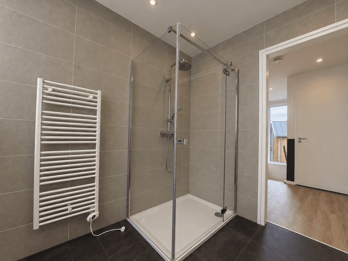 Douchecabine met glazen wanden, betegelde muren en een radiator in een ruime badkamer met houten vloer.