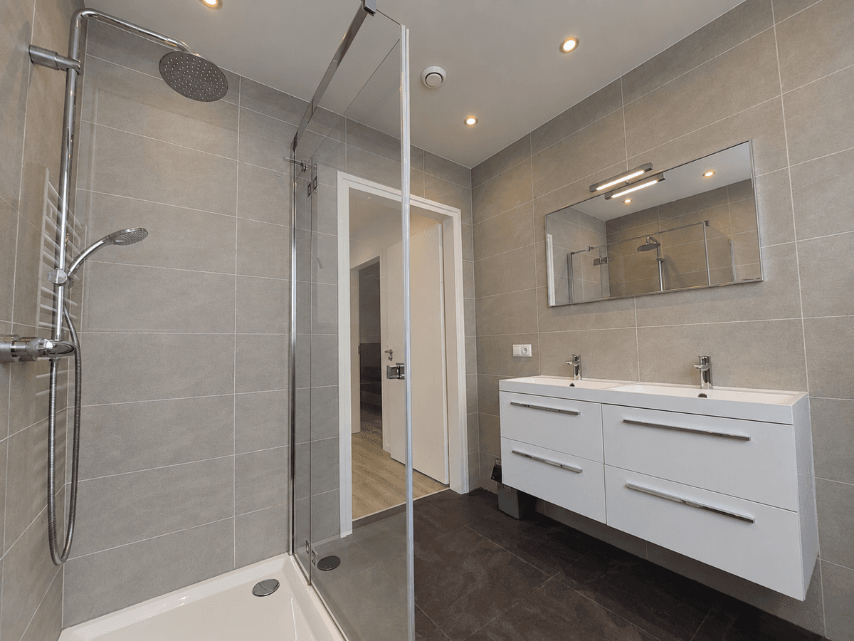 Moderne badkamer met inloopdouche, dubbele wastafel en grote spiegel, grijze wand- en vloertegels.