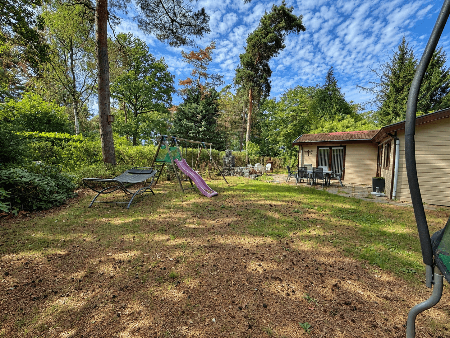 Zicht op een recreatiewoning met tuin, speeltoestellen en zitgroep in een groene omgeving bij RCN Vakantiepark de Flaasbloem.