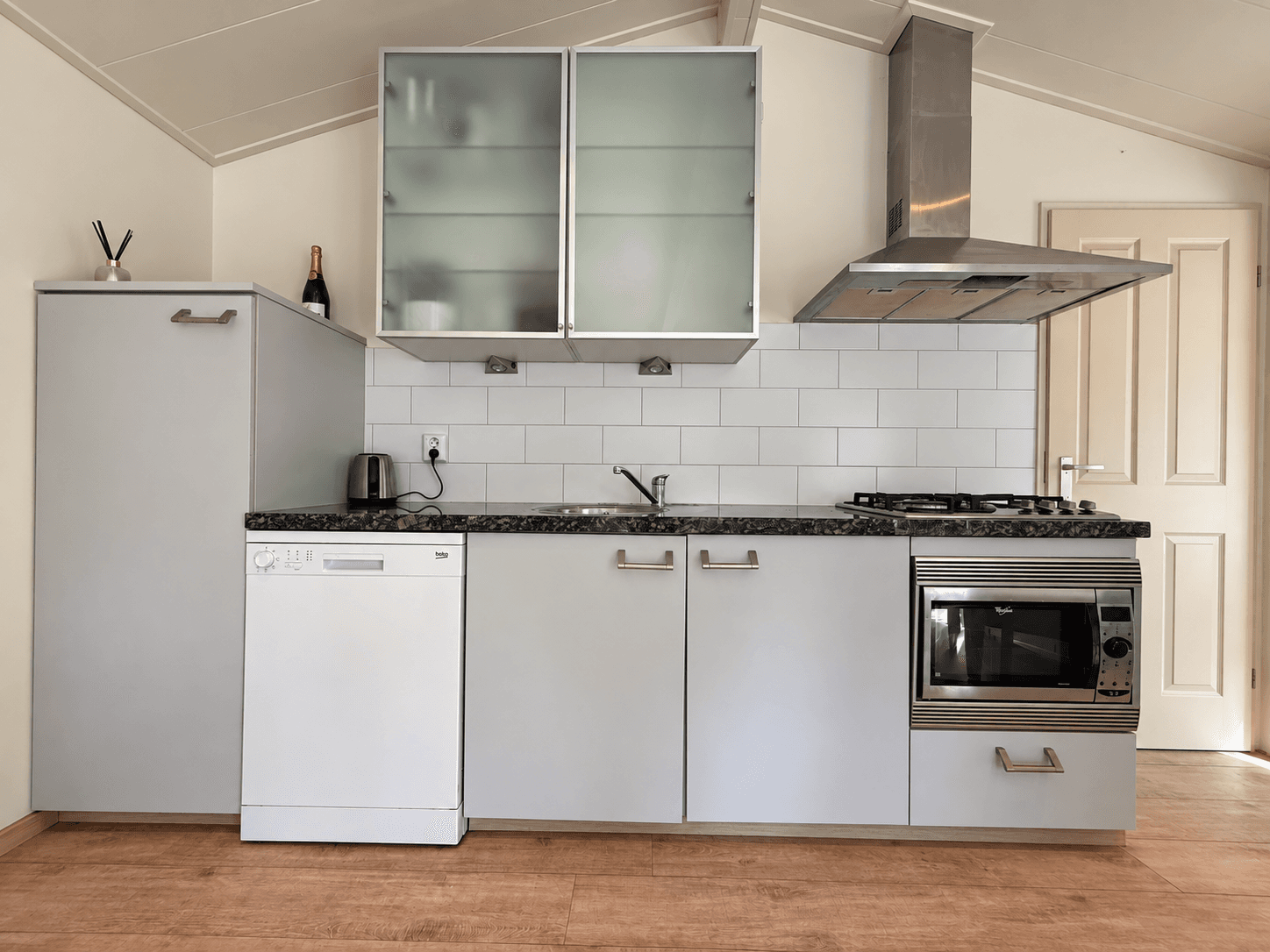 Keuken met moderne meubels, waaronder een vaatwasser, kookplaat en oven, afgewisseld met witte tegels en een granieten werkbl