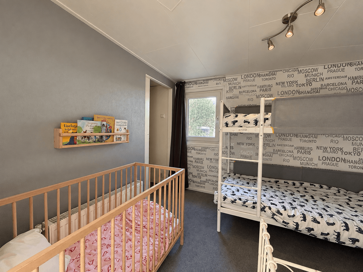 Slaapkamer met een ledikant en een stapelbed, muren met wereldsteden-thema en een raam met uitzicht naar buiten