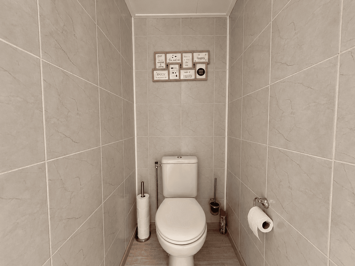 Toilet met betegelde wanden, toiletrolhouder en muurdecoratie boven het toilet
