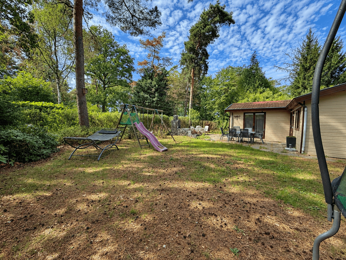 Zicht op een recreatiewoning met tuin, speeltoestellen en zitgroep in een groene omgeving bij RCN Vakantiepark de Flaasbloem.