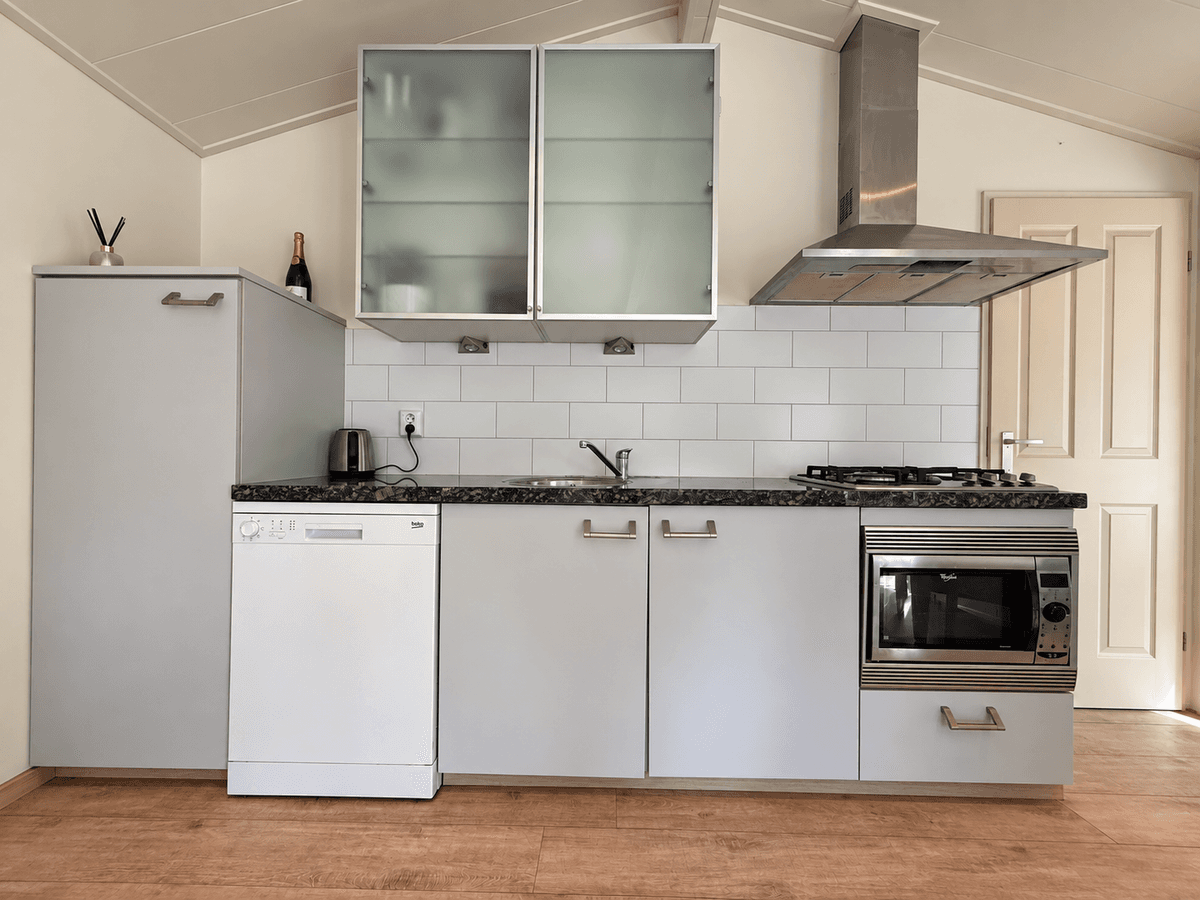 Keuken met moderne meubels, waaronder een vaatwasser, kookplaat en oven, afgewisseld met witte tegels en een granieten werkbl