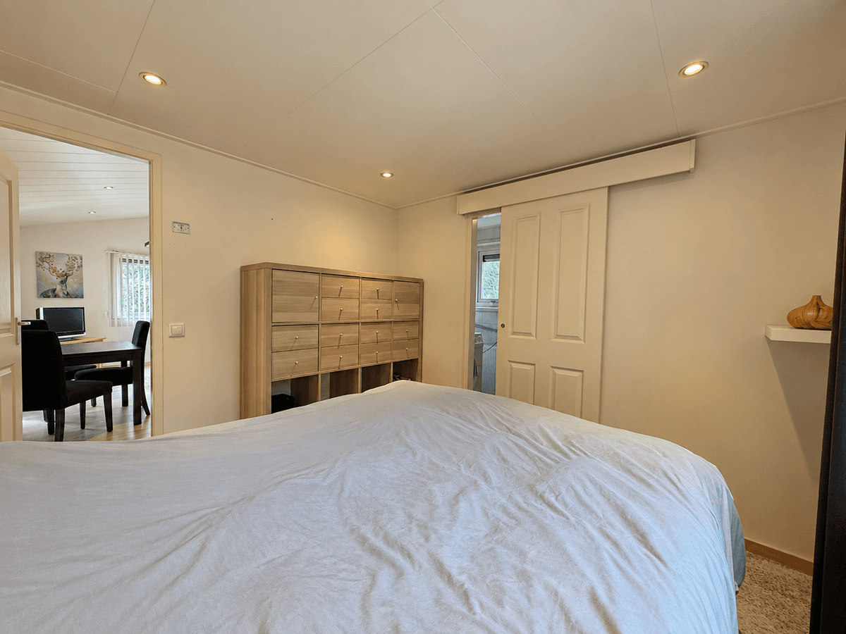 Sfeervolle slaapkamer met een groot bed, kastenwand en toegang tot een andere ruimte en badkamer