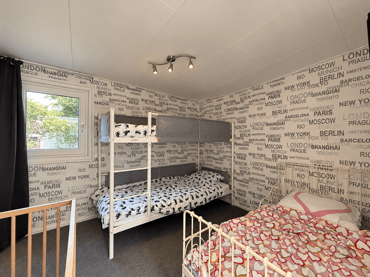Slaapkamer met stapelbed en eenpersoonsbed, muren bedekt met wereldsteden motief en raam met uitzicht naar buiten
