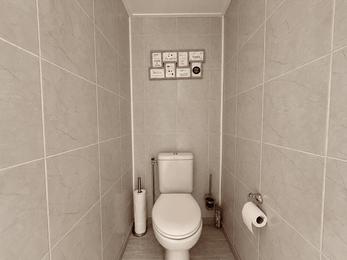 Toilet met betegelde wanden, toiletrolhouder en muurdecoratie boven het toilet
