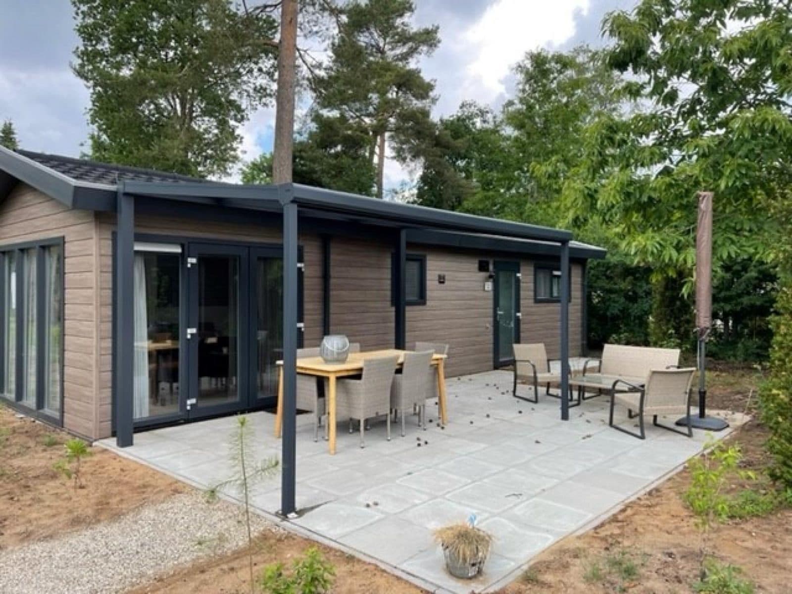 Recreatiewoning met een terras, tuinmeubilair en een moderne gevel, omringd door bomen op de Veluwe.