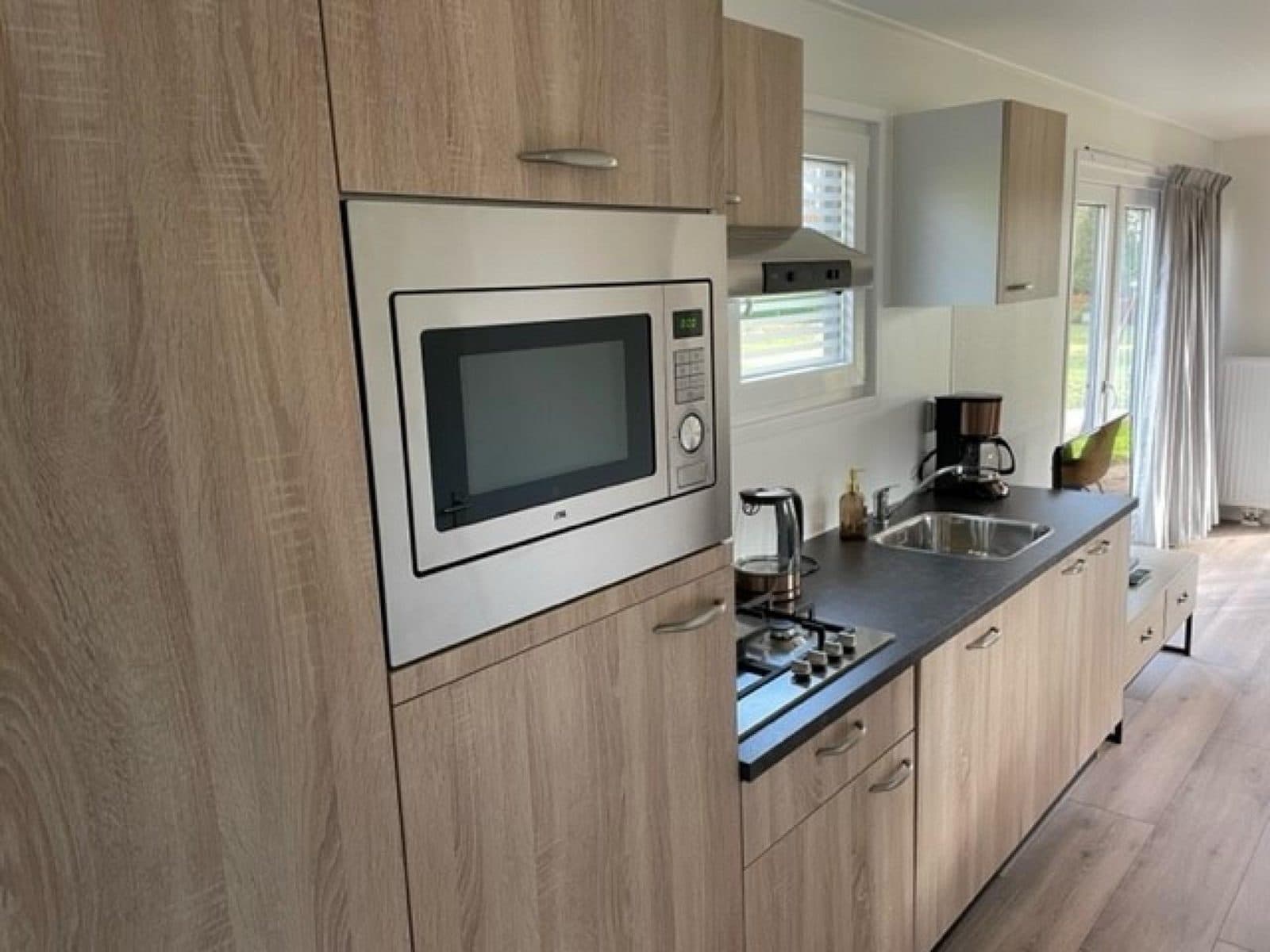 Moderne keuken met houten kasten, een ingebouwde magnetron, kookplaat en raampartij voor natuurlijk licht