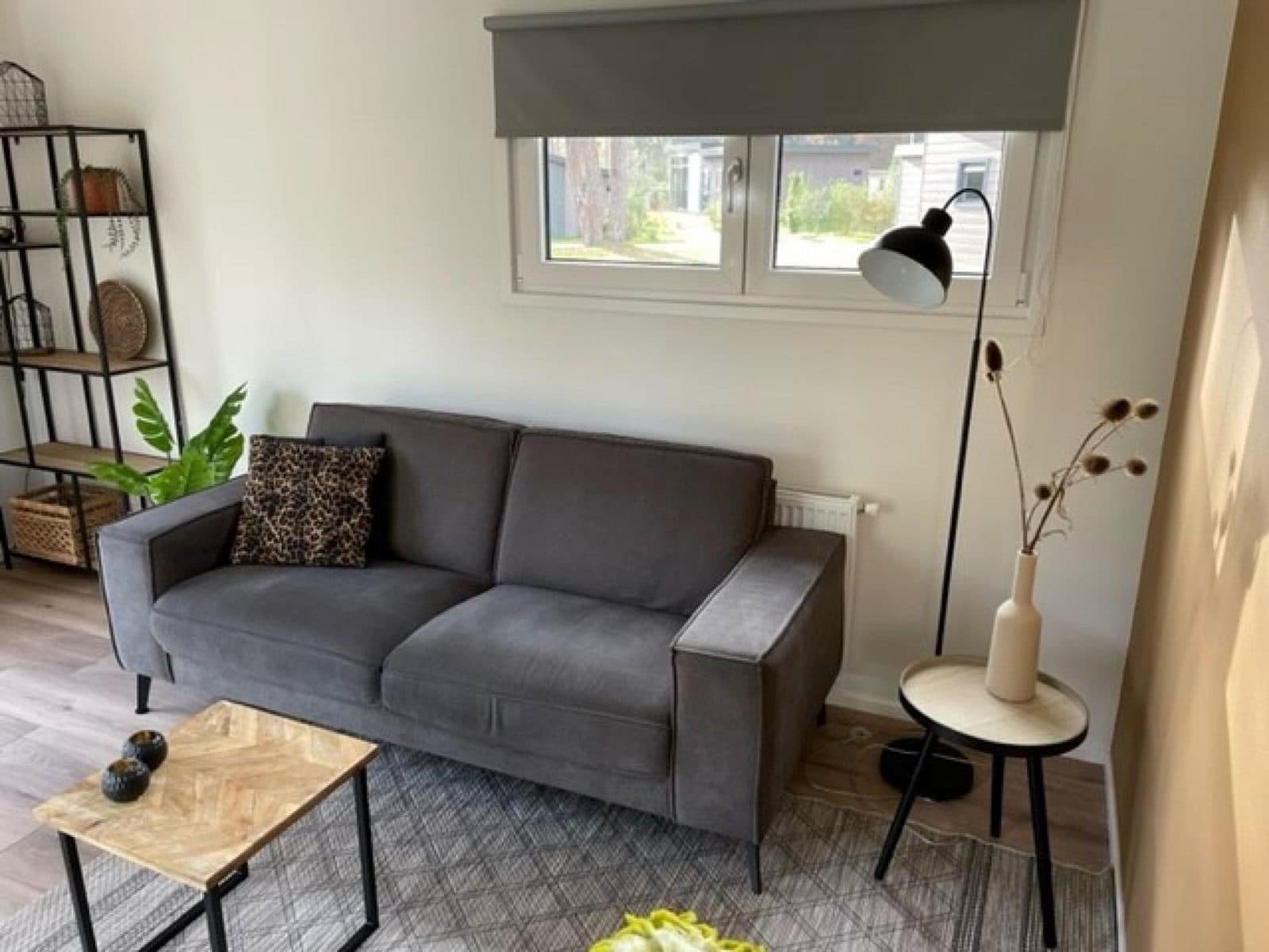 Zithoek met grijze bank, industriële lamp, planten en decoratieve elementen zoals een vaas en twee schalen