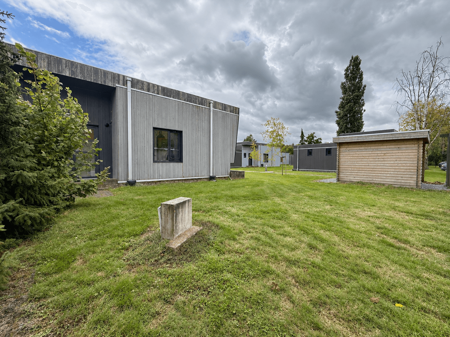 Recreatiewoningen met houten gevels en een groene tuin in het vakantiecentrum 't Schuttenbelt, onder een bewolkte lucht