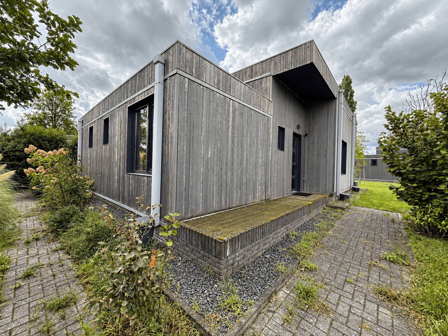 Moderne recreatiewoning met houten gevel, kleine veranda en groenvoorziening rondom, gelegen op vakantiecentrum 't Schuttenbe