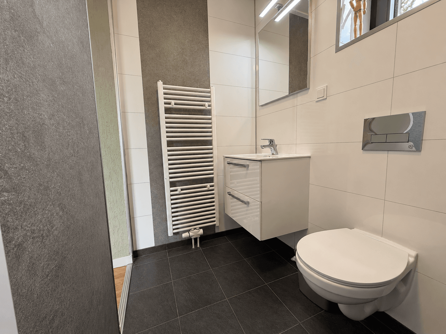 Moderne badkamer met muurverwarming, wastafel met opberglades en een toilet, lichtgekleurde tegels en zwarte vloertegels
