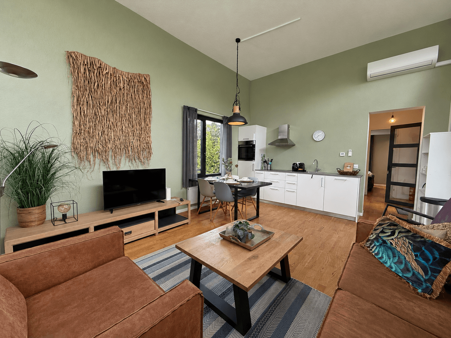 Woonkamer met groene muren, bankstel, salontafel en open keuken met eettafel en moderne apparatuur