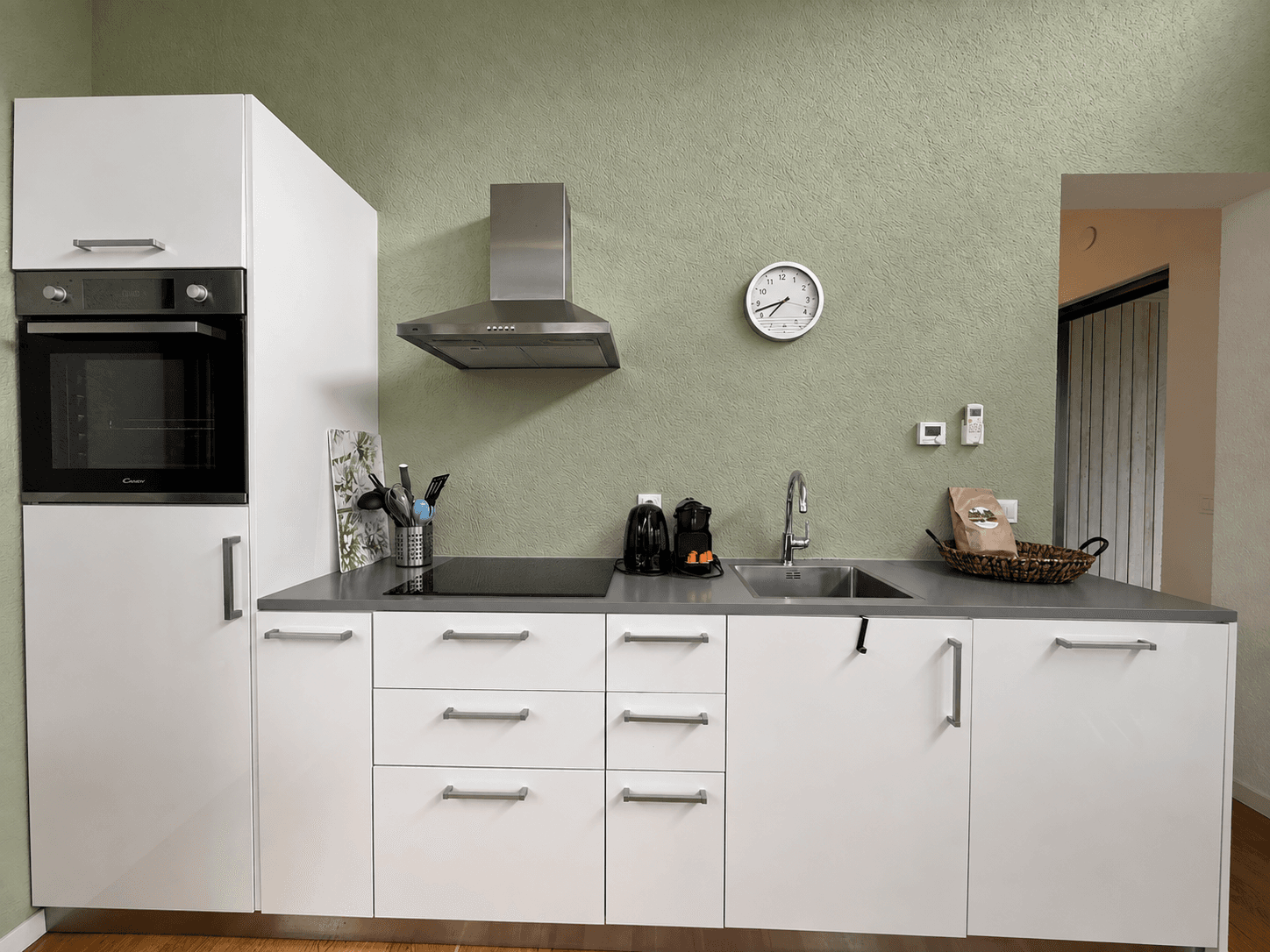 Moderne keuken met witte kastjes, roestvrijstalen aanrecht en inbouwapparaten zoals een oven en afzuigkap