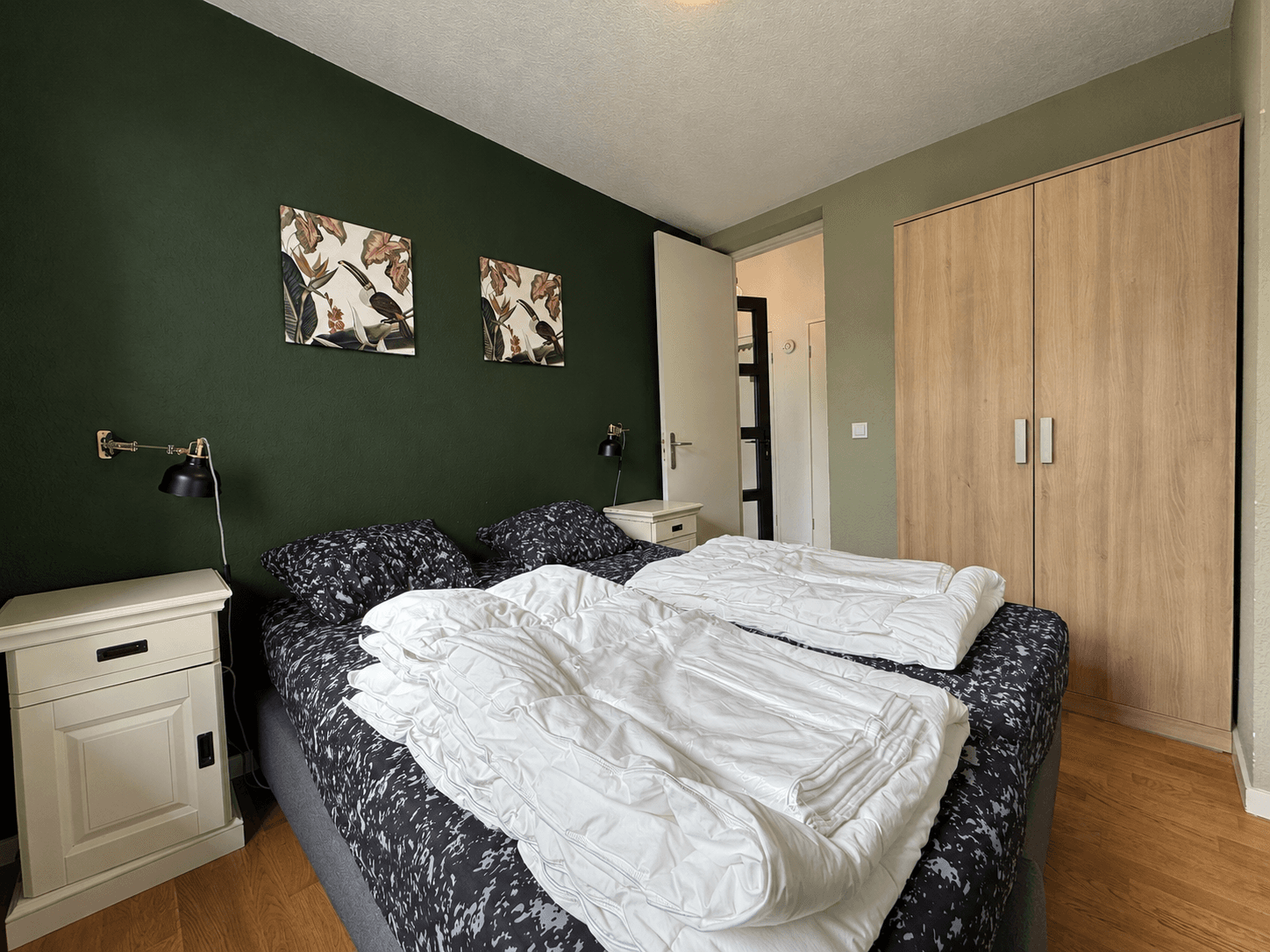 Slaapkamer met twee eenpersoonsbedden, nachtkastjes, een kastenwand en groene muren.
