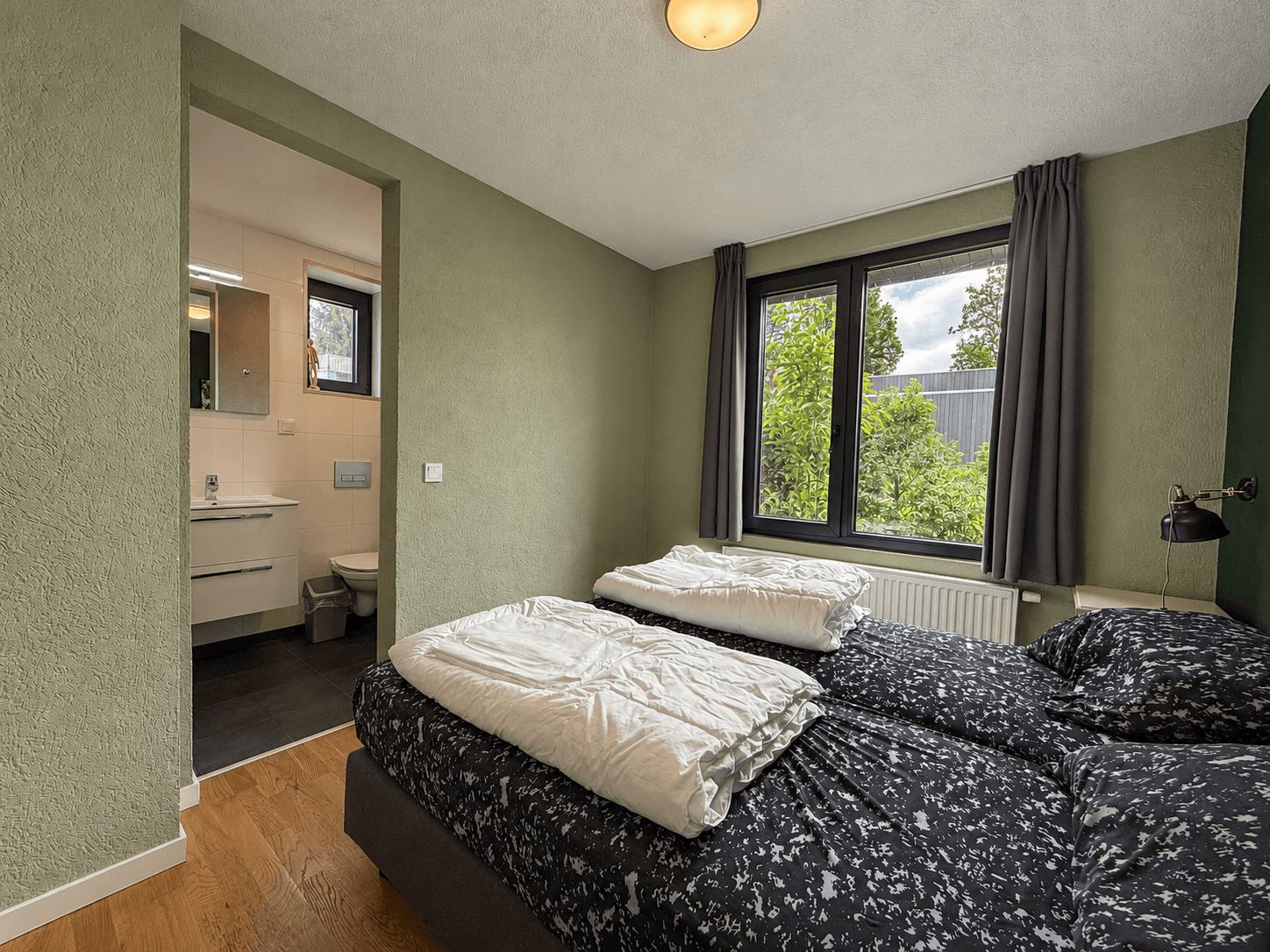 Slaapkamer met twee eenpersoonsbedden, raam met uitzicht op groen, connectie naar badkamer zichtbaar.