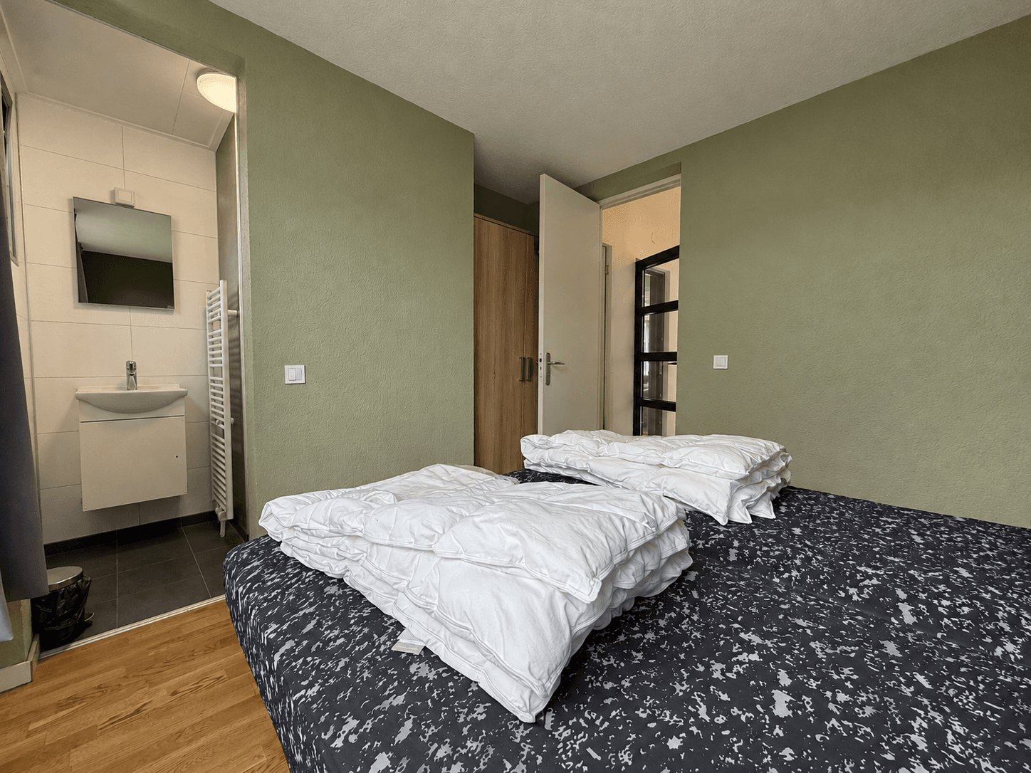Slaapkamer met twee bedden, een wastafel met spiegel en een open kast in de buurt van de deur.