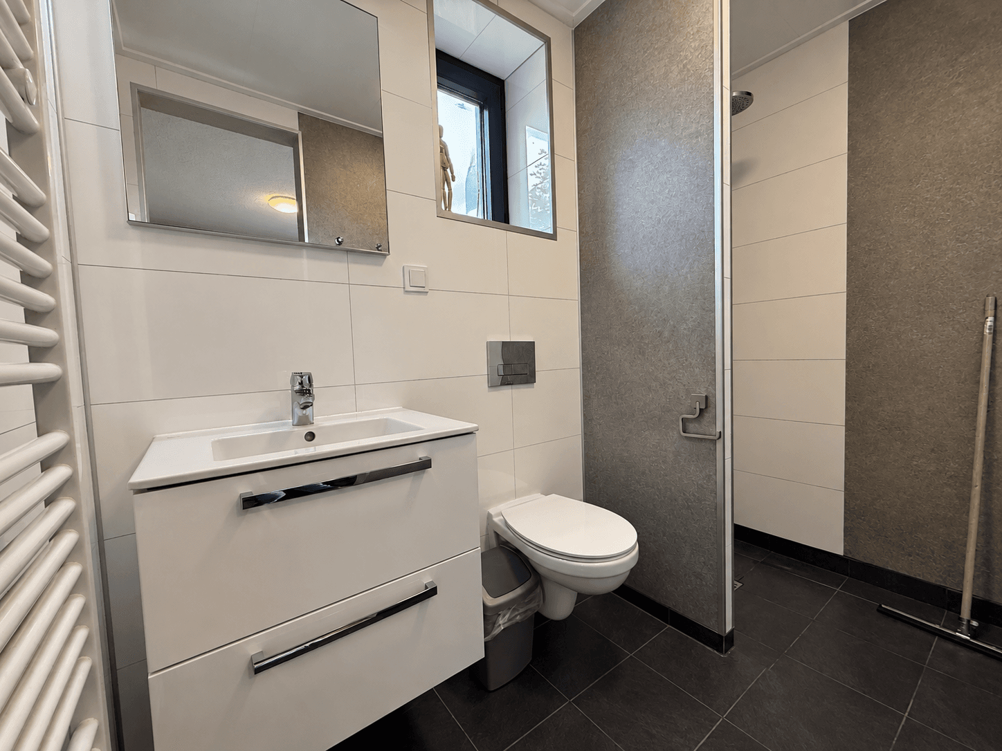 Moderne badkamer met wastafel, toilet, douche en handdoekradiator in neutrale kleuren.
