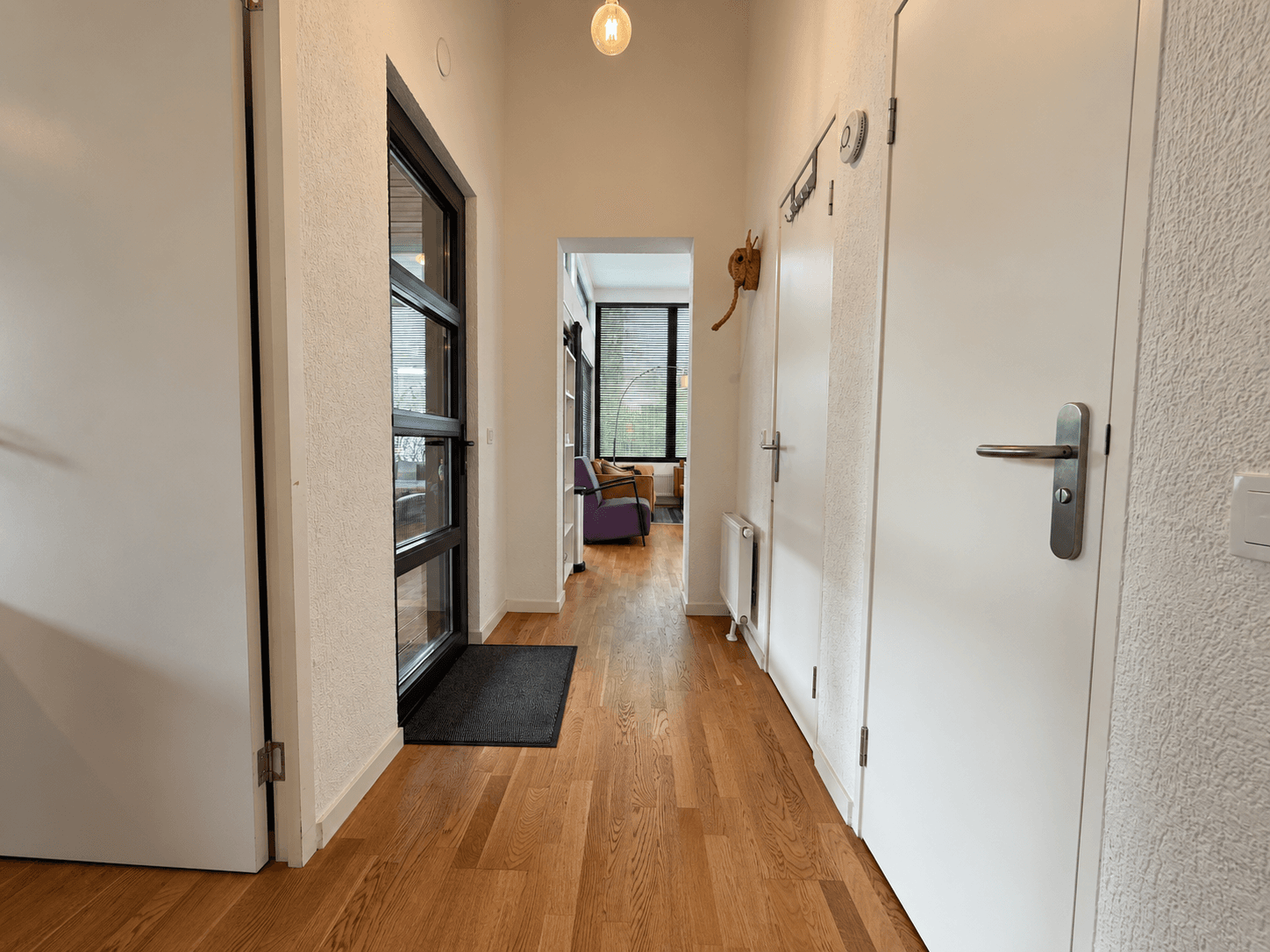 Entreehal van een recreatiewoning met houten vloer, wanden in lichte kleur en deuren aan beide zijden, met toegang tot woonka