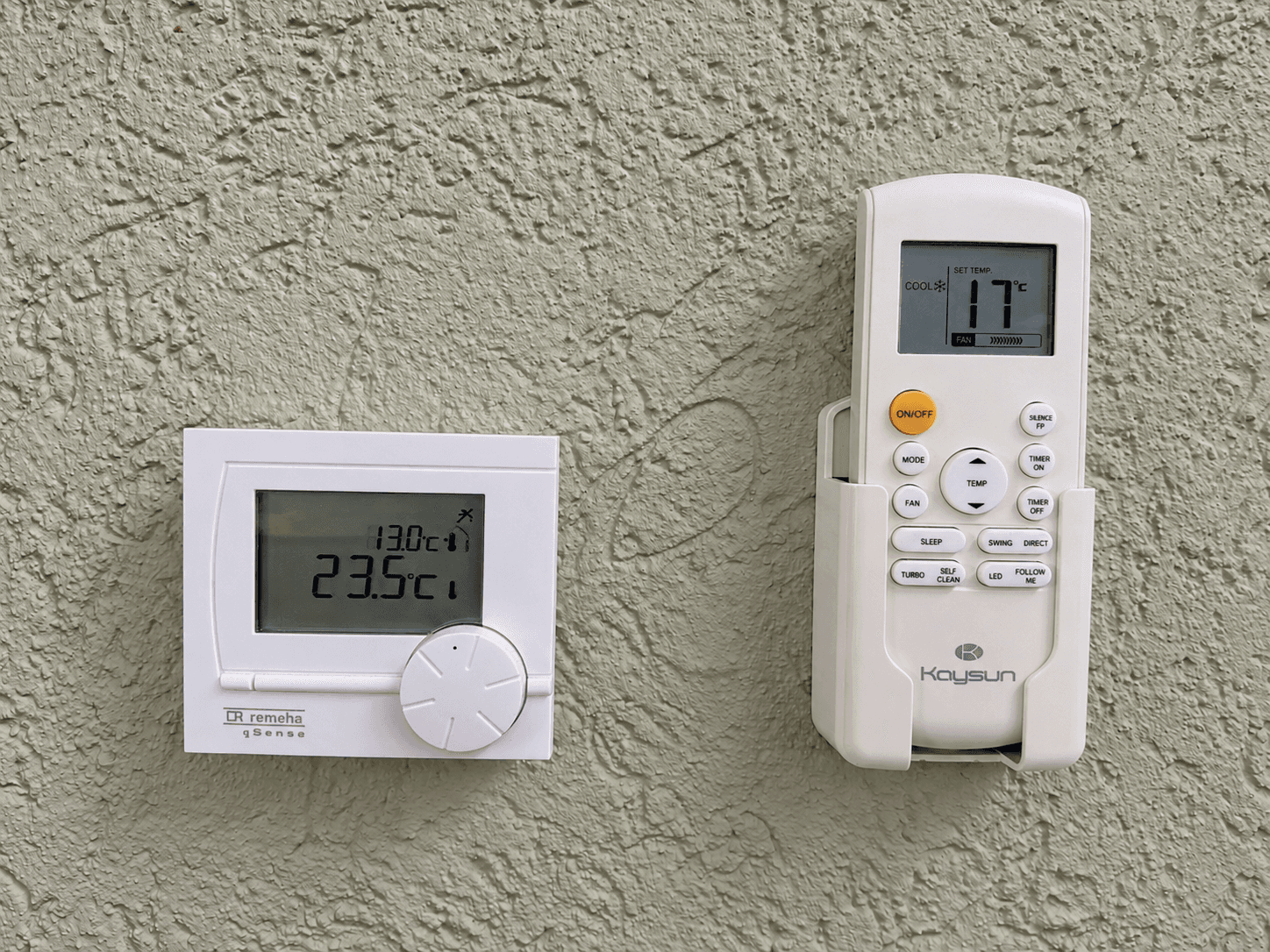 Thermostaten aan de muur met verschillende temperaturen weergegeven, witte en grijze toestellen op een lichtgroene wand