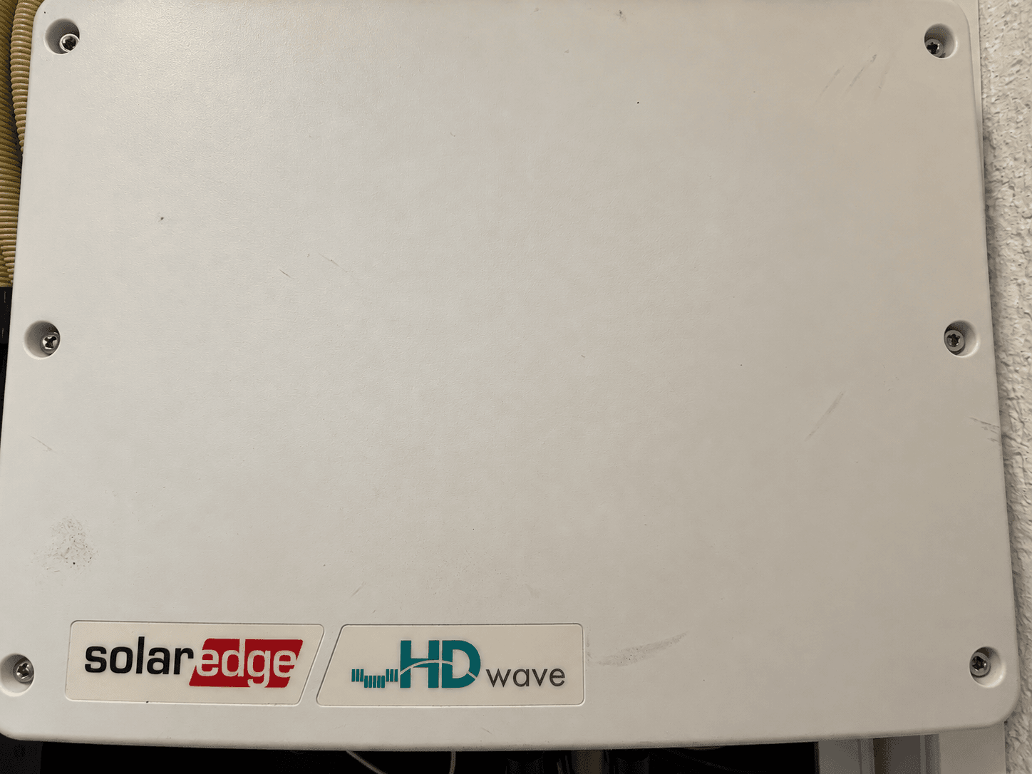 Zicht op een witte kast met logo's van SolarEdge en HD Wave, bevestigd aan een wand.