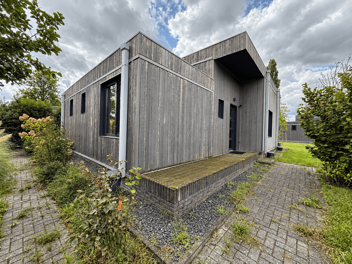 Moderne recreatiewoning met houten gevel, kleine veranda en groenvoorziening rondom, gelegen op vakantiecentrum 't Schuttenbe
