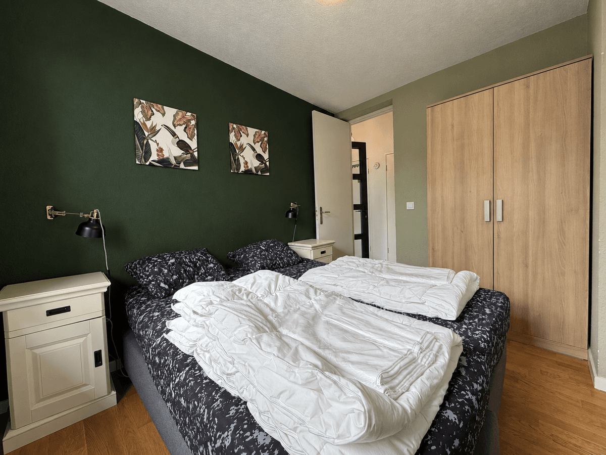 Slaapkamer met twee eenpersoonsbedden, nachtkastjes, een kastenwand en groene muren.