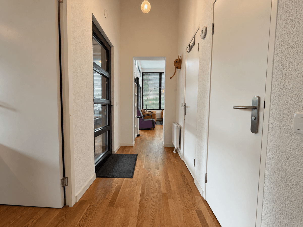 Entreehal van een recreatiewoning met houten vloer, wanden in lichte kleur en deuren aan beide zijden, met toegang tot woonka