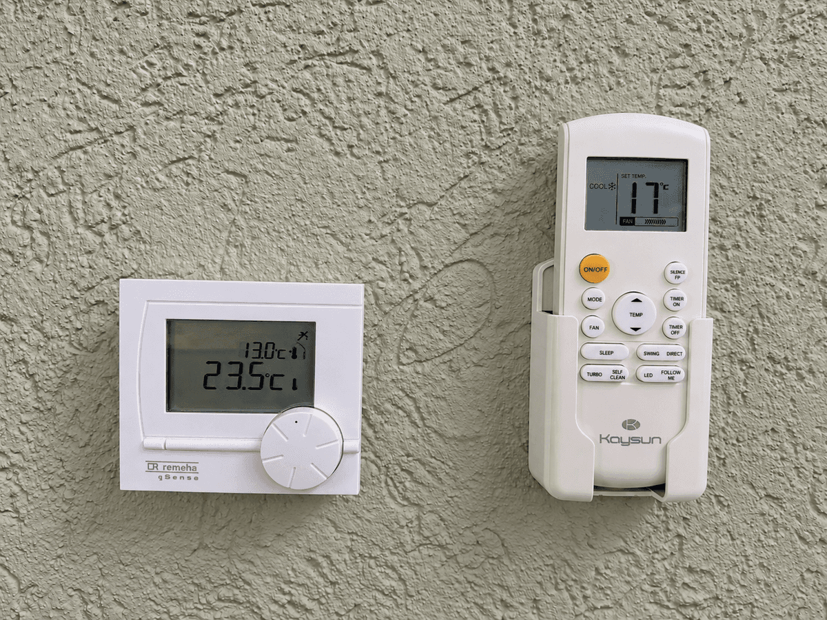 Thermostaten aan de muur met verschillende temperaturen weergegeven, witte en grijze toestellen op een lichtgroene wand