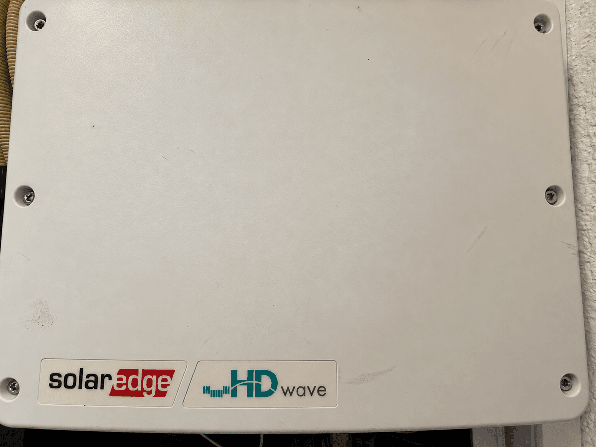 Zicht op een witte kast met logo's van SolarEdge en HD Wave, bevestigd aan een wand.