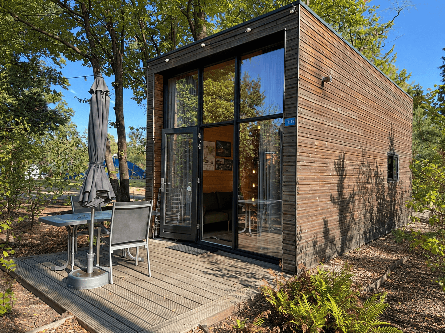 Moderne recreatiewoning met houten gevel, terras met tuinmeubilair en grote ramen in groene omgeving