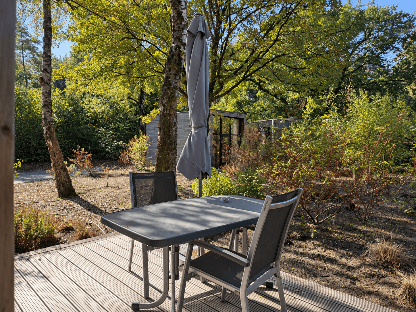 Terras met houten vlonders en een tafel met stoelen, omringd door groen en bomen in een rustige omgeving