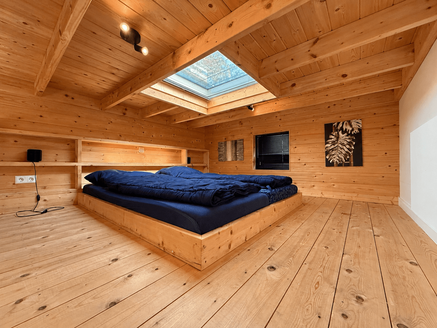 Houten slaapkamer met schuin plafond, dakraam en een groot tweepersoonsbed op een houten vloer