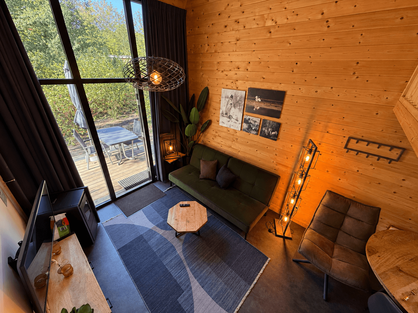 Gezellige woonkamer met houten wand, bank, salontafel en grote ramen met uitzicht op het terras buiten.