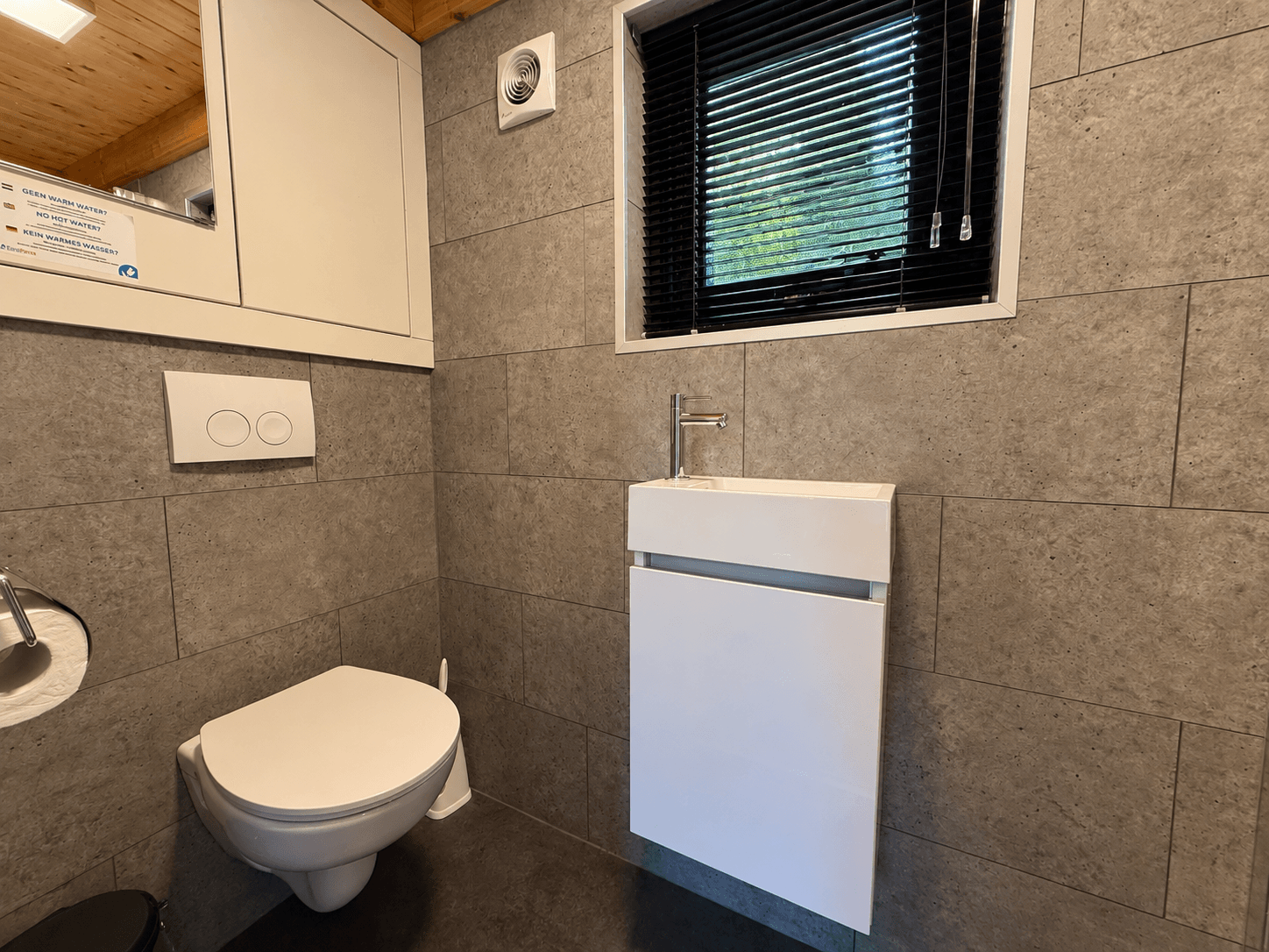 Modern toilet met wandmeubel en kleine venster met zwarte jaloezieën in een betegelde ruimte